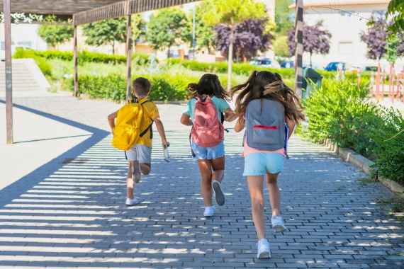 Kinder, die über einen breiten Gehweg laufen, im Hintergrund eine Pergola mit Beschattung, auf der Seite Begrünung