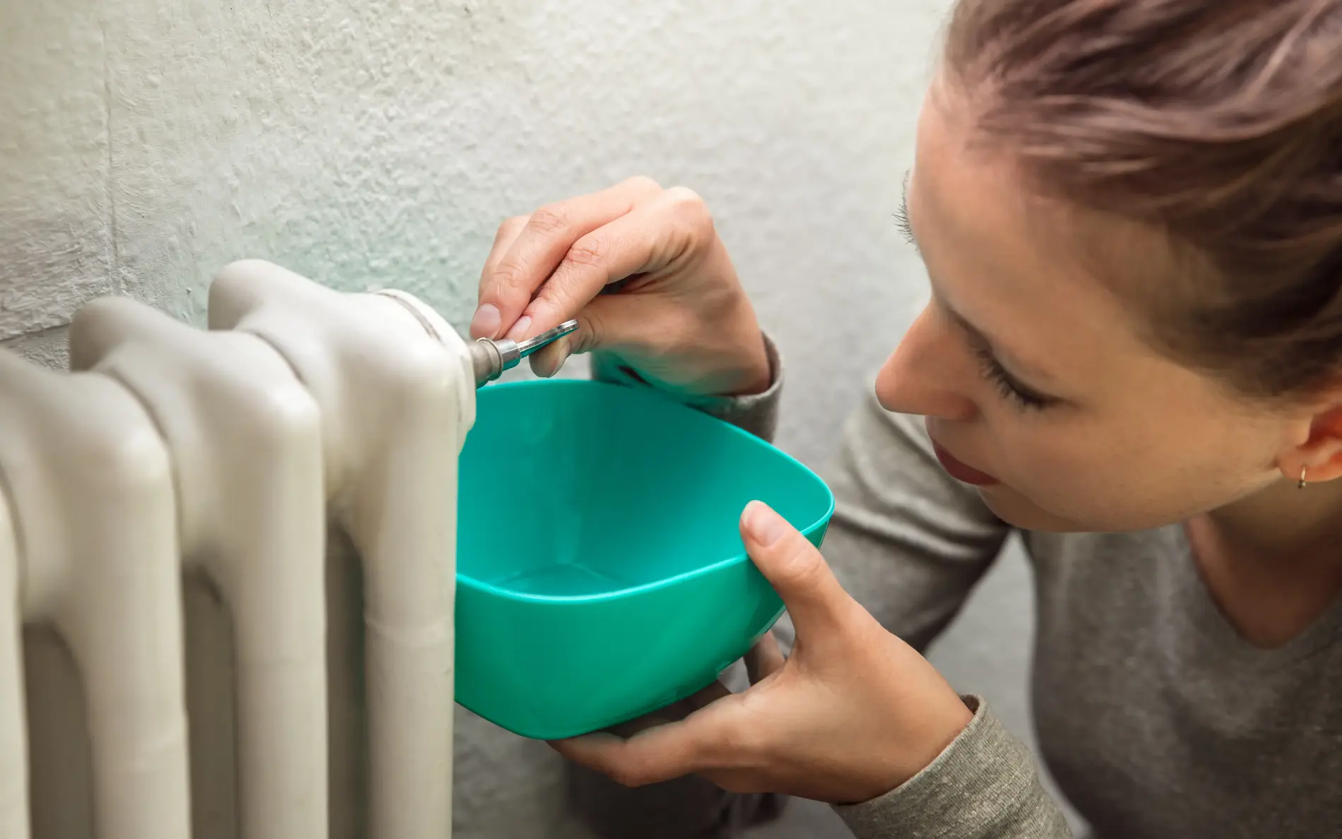 Eine Frau lässt Wasser aus der Heizung ab und fängt es mit einer Plastikschüssel auf