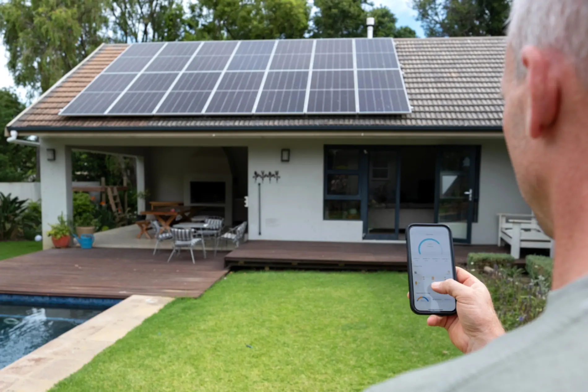 Zu sehen ist ein Mann von hinten der sein Handy in der Hand hat und Richtung seiner PV-Anlage am Dach schaut.