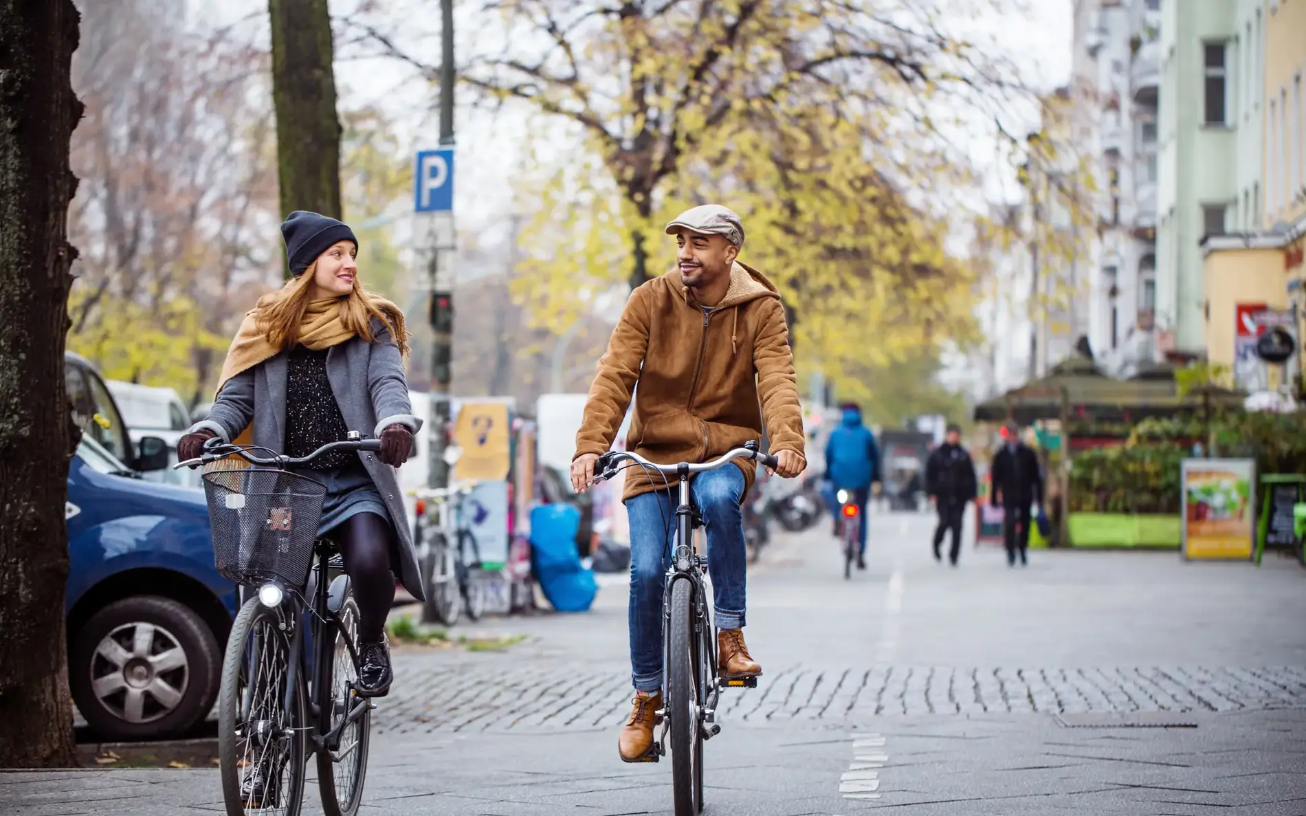 Zwei Personen radeln nebeneinander auf einer breiten Straße. Sie tragen Winterkleidung.