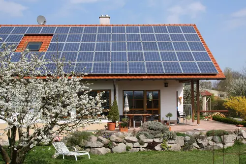 Solaranlage auf dem Dach eines Einfamilienhauses. Davor ein Garten