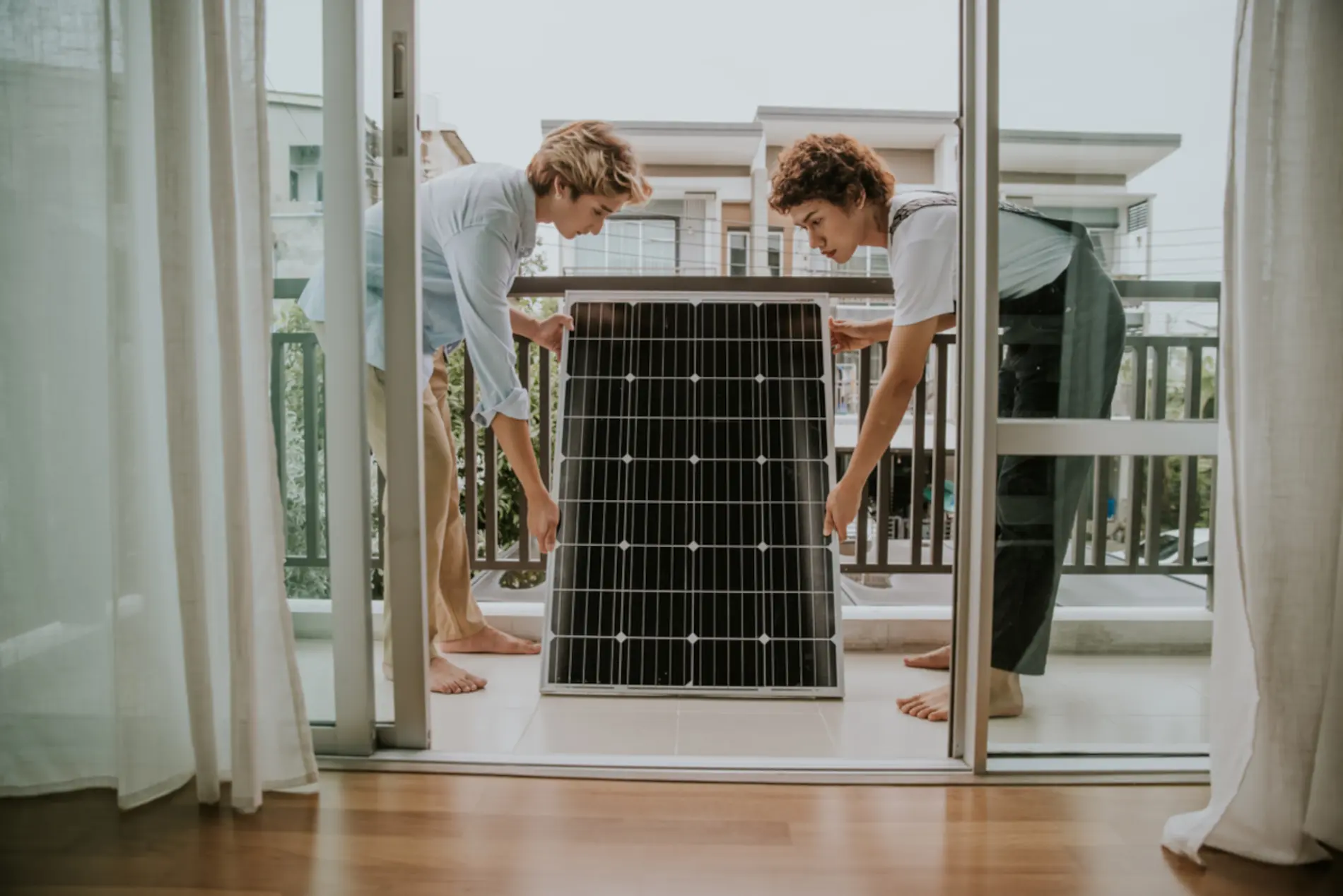 Zu sehen sind zwei Frauen auf einem Balkon die gemeinsam ein PV Panel halten.