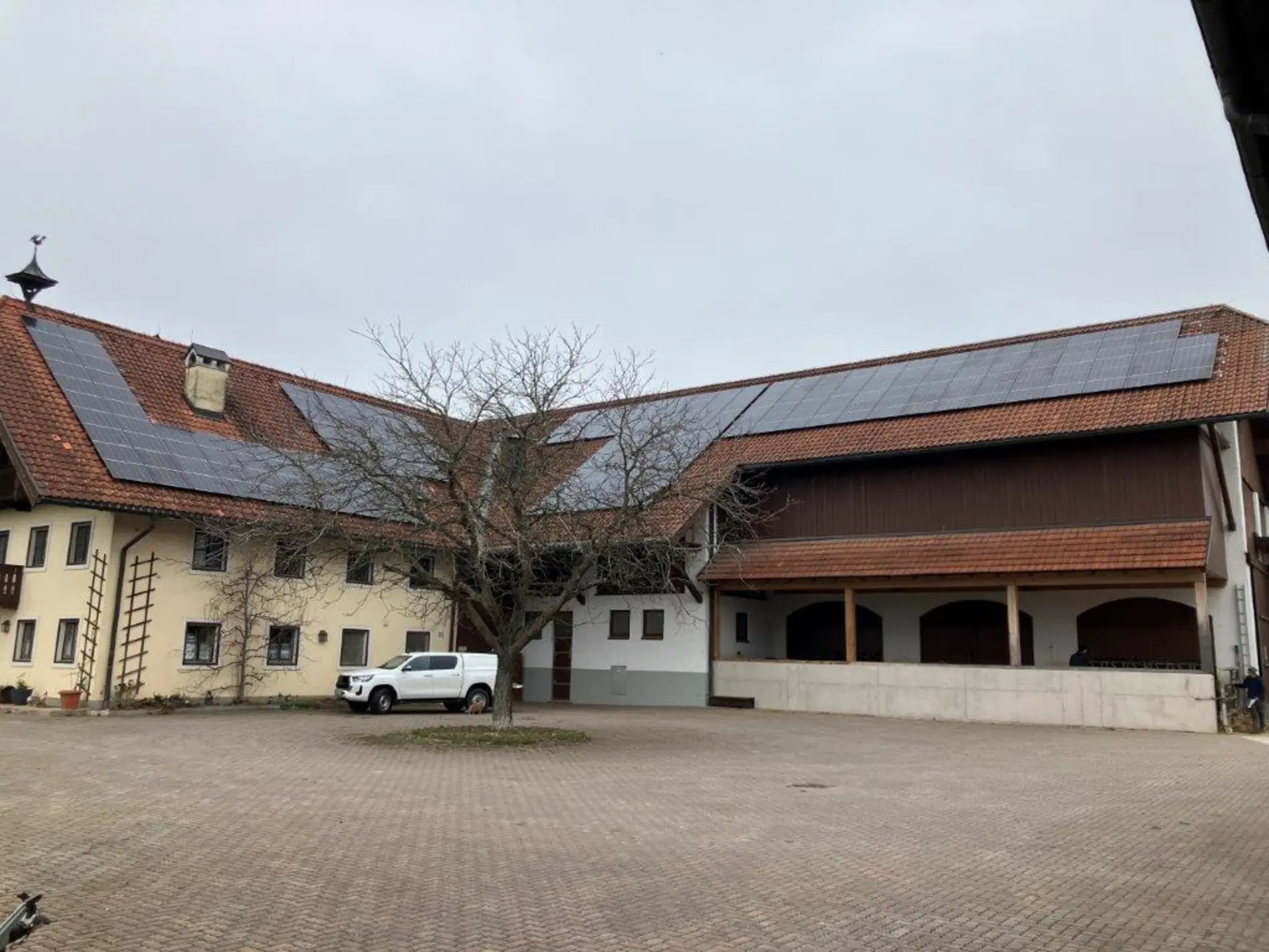 PV-Anlage auf den beiden Dächern des Miedering-Hofes, ein L-förmig gebauter Hof mit einem großen gepflasterten Vorplatz 