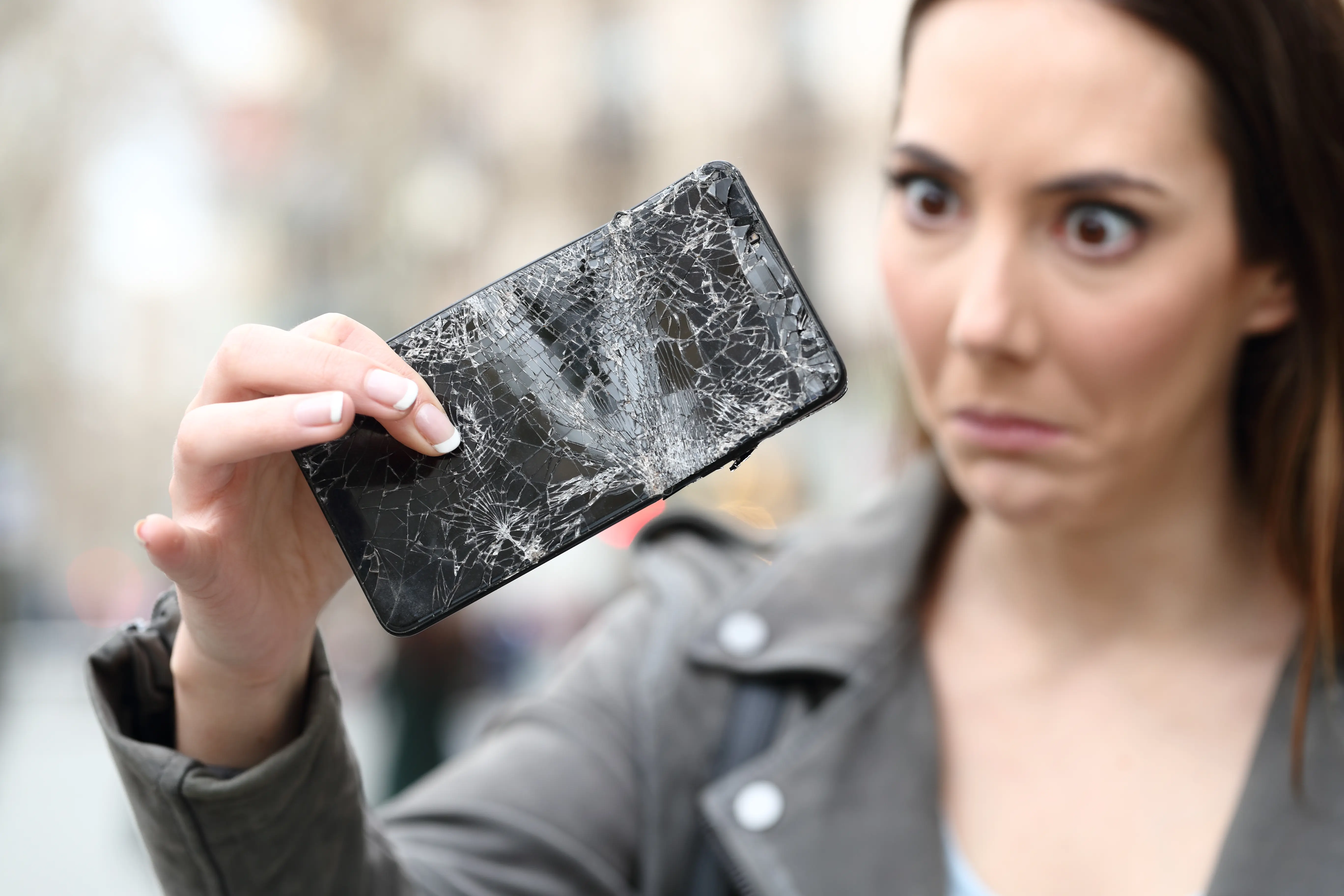 Frau hält Handy mit kaputtem Display in der Hand