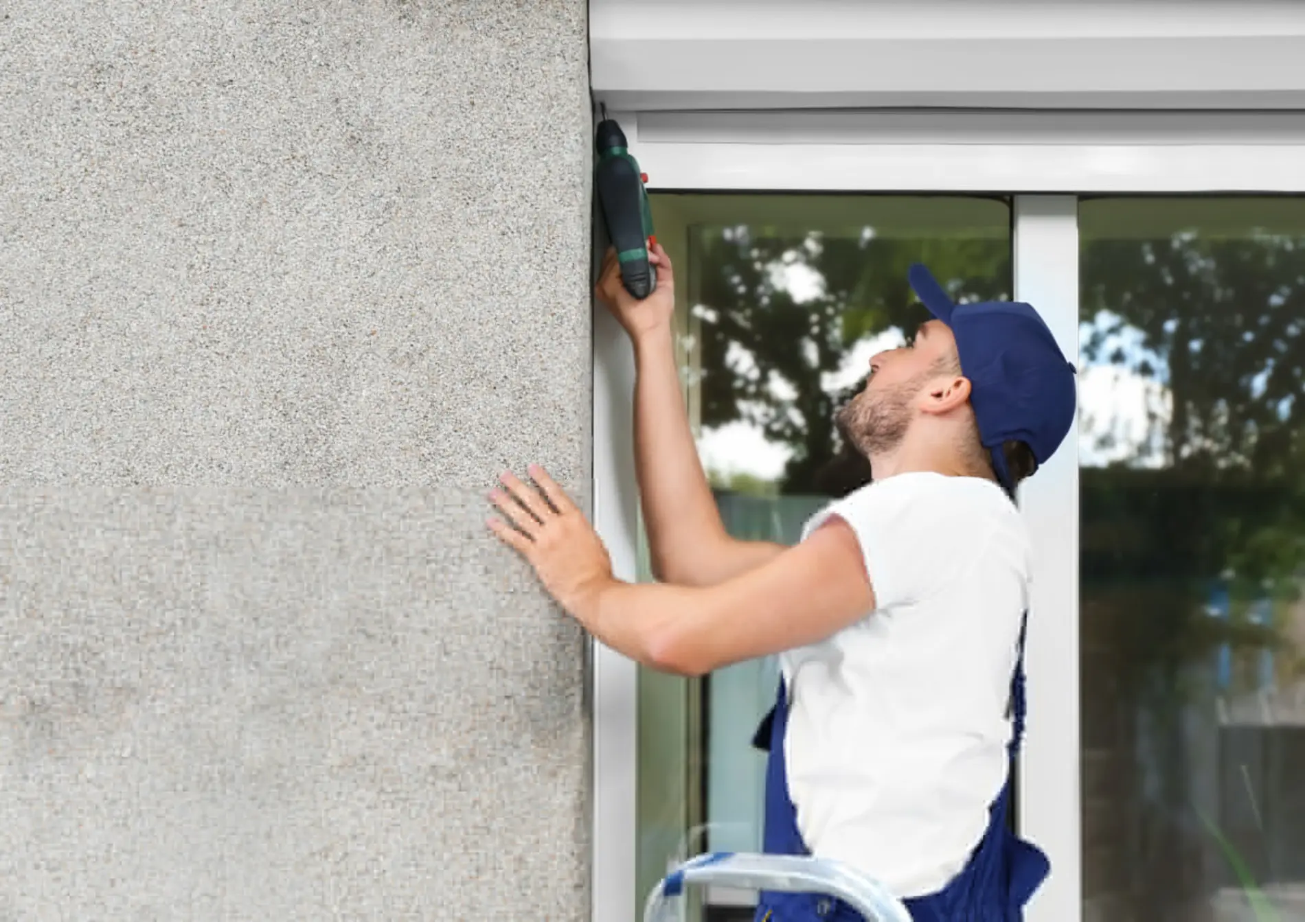 Ein Arbeiter montiert vor einem Fenster eine Außenjalousie