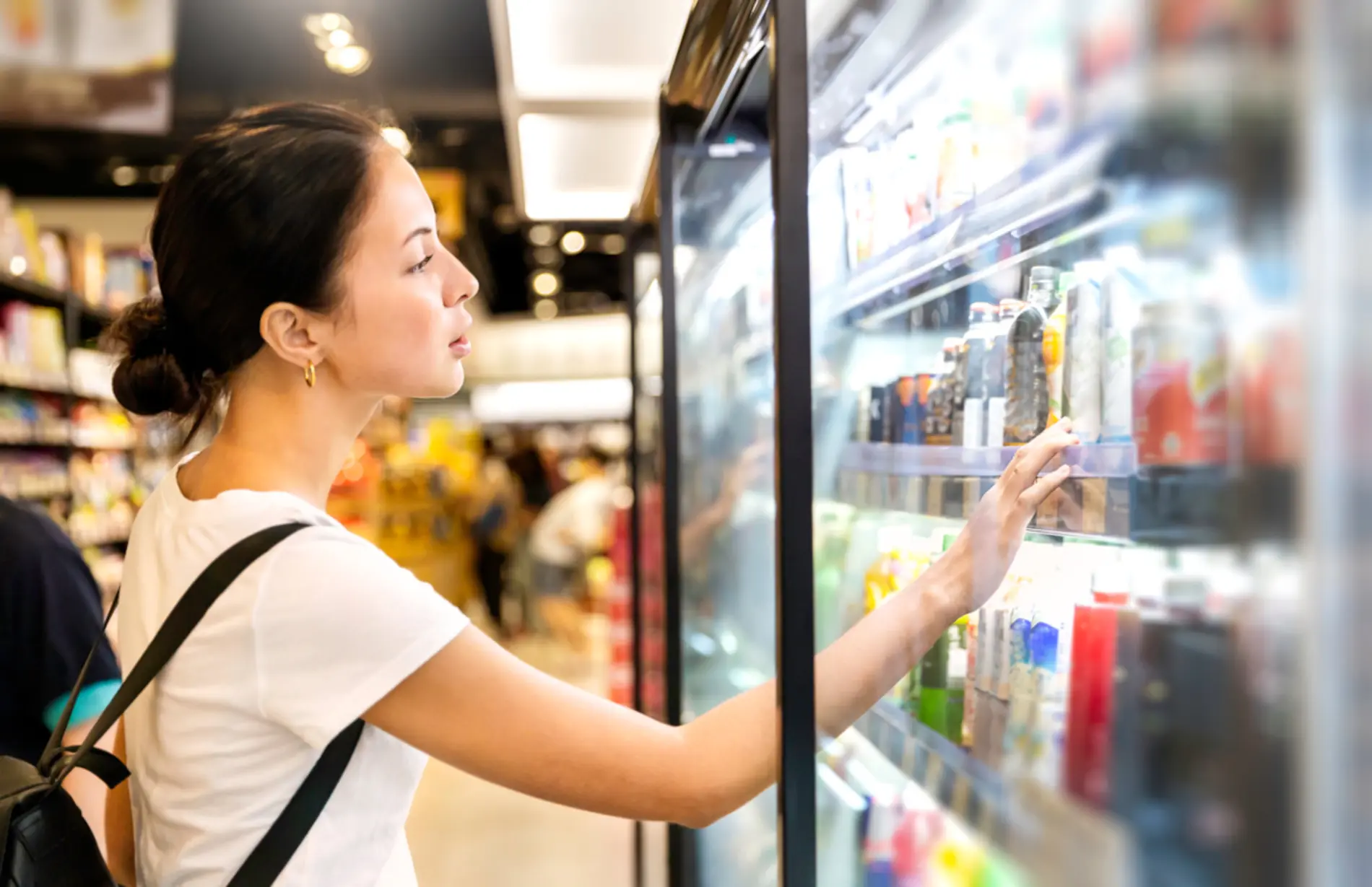 Eine Frau steht vor einem Kühlregal im Supermarkt und schaut sich verschiedenste Flaschen an